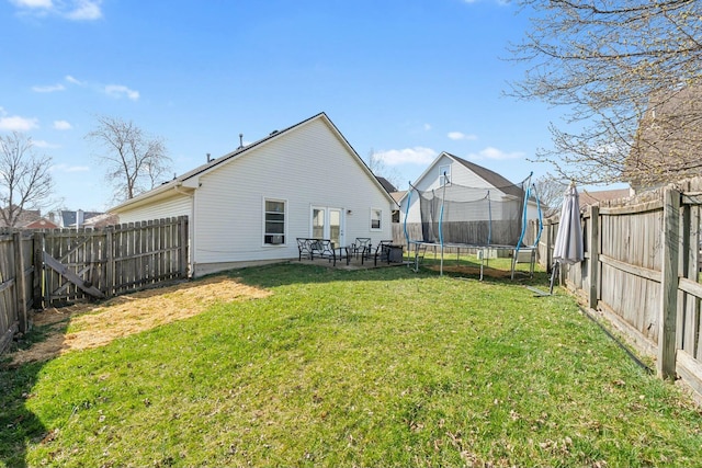 back of house with a fenced backyard, a lawn, and a trampoline