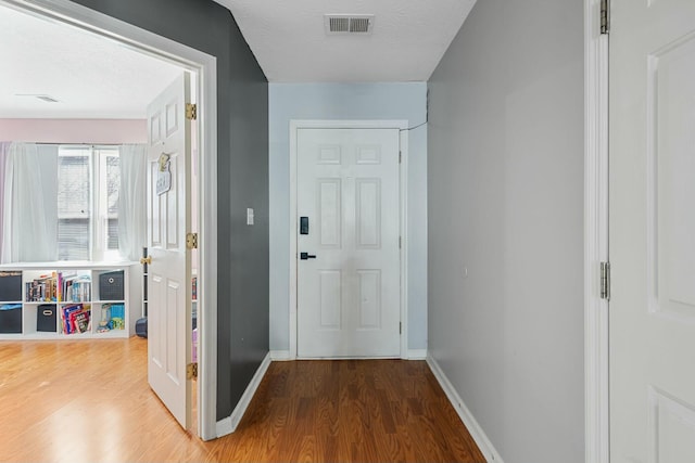 hallway featuring visible vents, baseboards, a textured ceiling, and wood finished floors