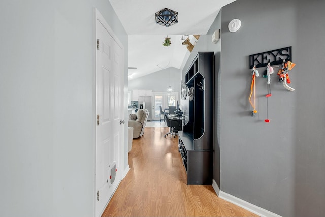 hall with vaulted ceiling, light wood-style flooring, and baseboards