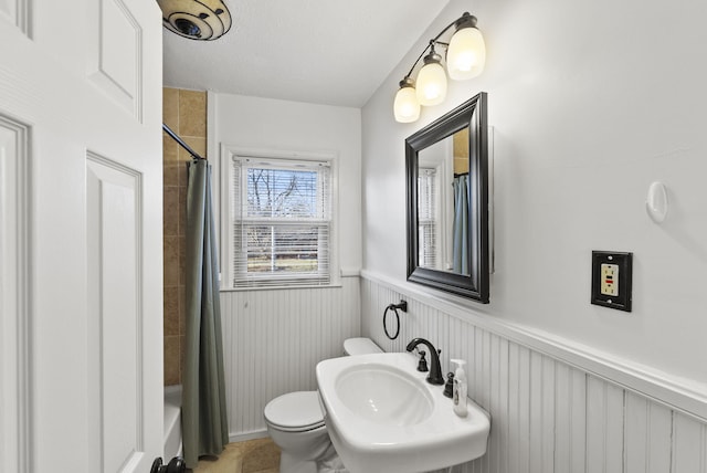 full bath featuring a wainscoted wall, toilet, shower / tub combo with curtain, a textured ceiling, and a sink