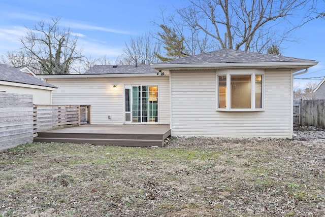 rear view of house featuring a shingled roof, a deck, and fence