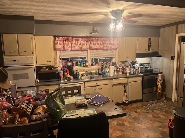 kitchen with a ceiling fan, a sink, stainless steel appliances, stone finish floor, and under cabinet range hood