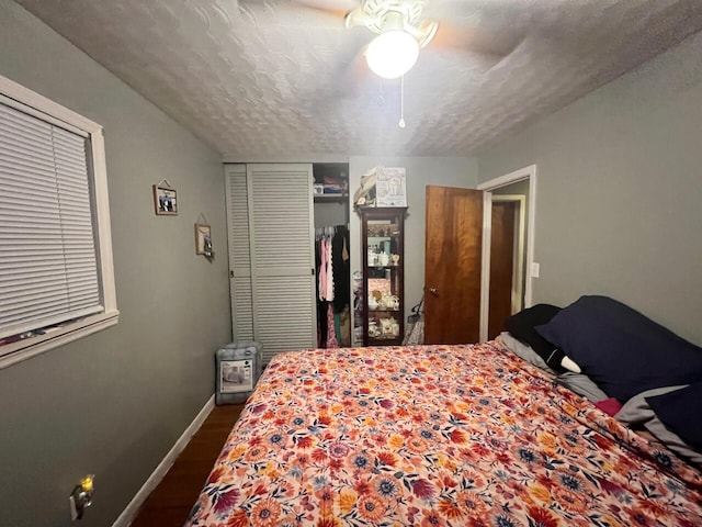 bedroom featuring dark wood-type flooring, baseboards, a closet, a textured ceiling, and a ceiling fan