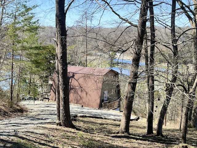 view of property exterior featuring a gambrel roof, metal roof, and a view of trees