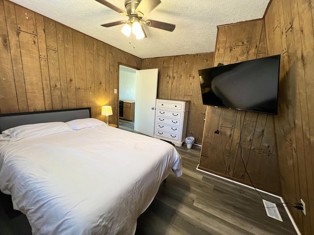 bedroom featuring wooden walls, dark wood-style floors, a ceiling fan, and a textured ceiling