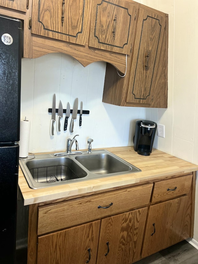 kitchen featuring a sink, wooden counters, brown cabinetry, and freestanding refrigerator