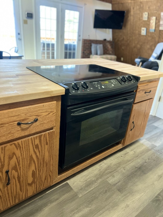 kitchen with brown cabinetry, black / electric stove, wood finished floors, and wood counters