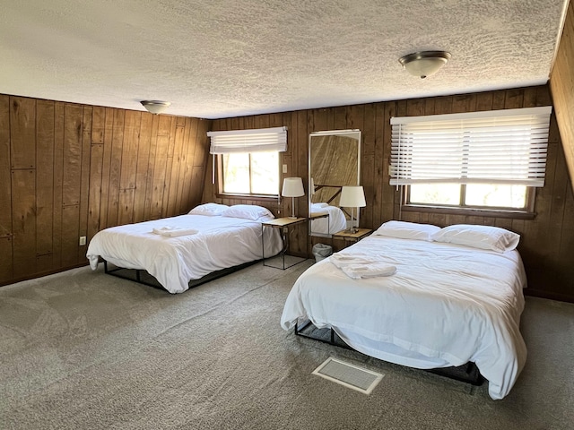 bedroom with carpet flooring, visible vents, a textured ceiling, and wooden walls