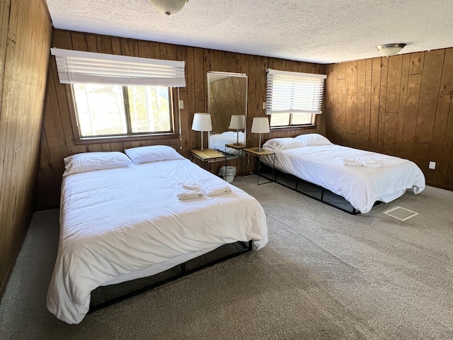 carpeted bedroom with visible vents, a textured ceiling, and wooden walls