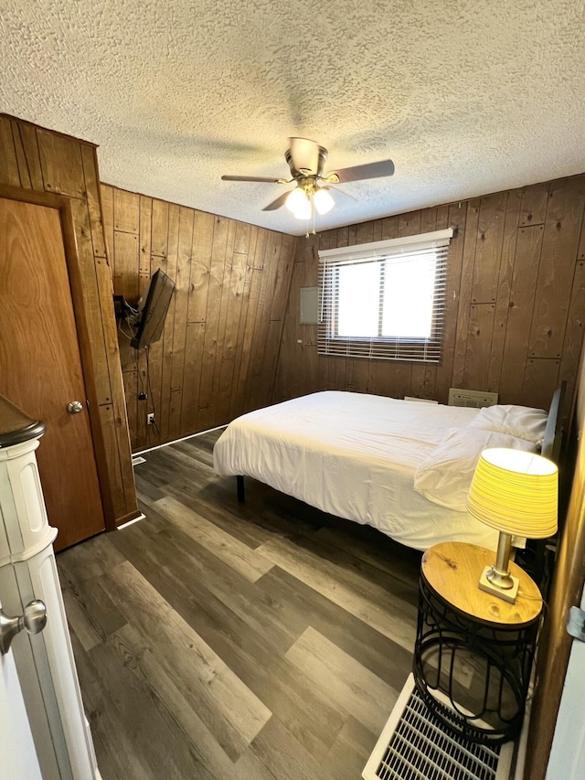 bedroom featuring a ceiling fan, dark wood-style flooring, wood walls, and a textured ceiling