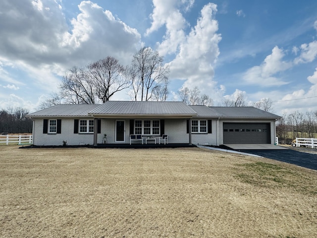 ranch-style home featuring fence, driveway, an attached garage, brick siding, and metal roof