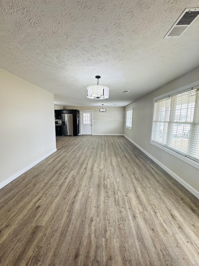 unfurnished living room with visible vents, a textured ceiling, baseboards, and wood finished floors