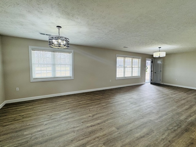 unfurnished dining area with baseboards, visible vents, dark wood-style flooring, a textured ceiling, and a chandelier