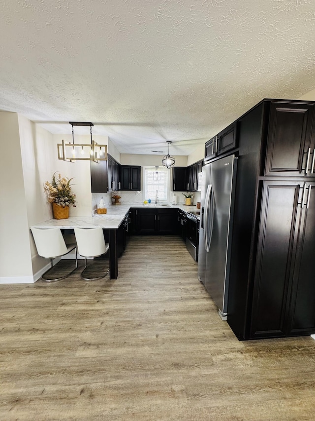 kitchen featuring light wood finished floors, a textured ceiling, dark cabinetry, stainless steel fridge, and light countertops