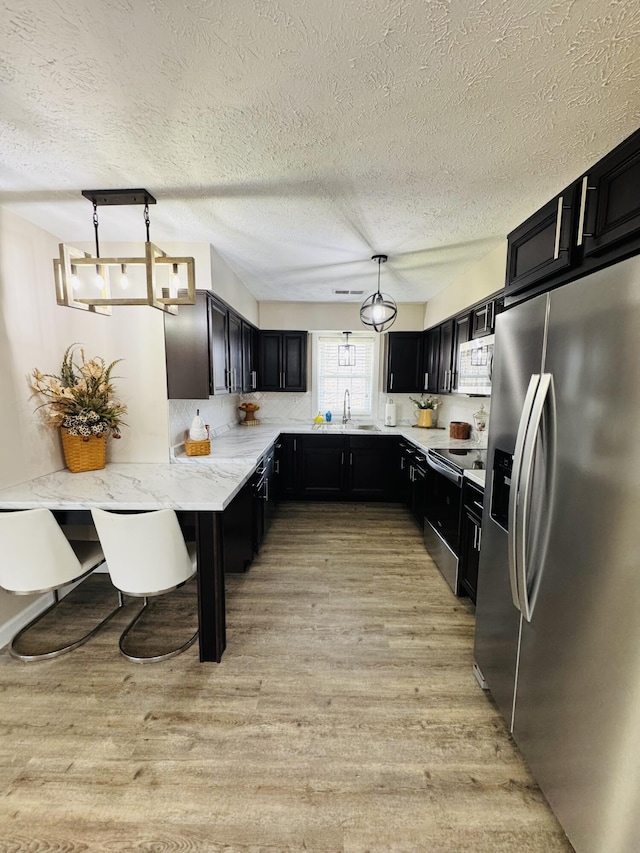 kitchen featuring light wood-style flooring, a sink, decorative light fixtures, appliances with stainless steel finishes, and dark cabinets