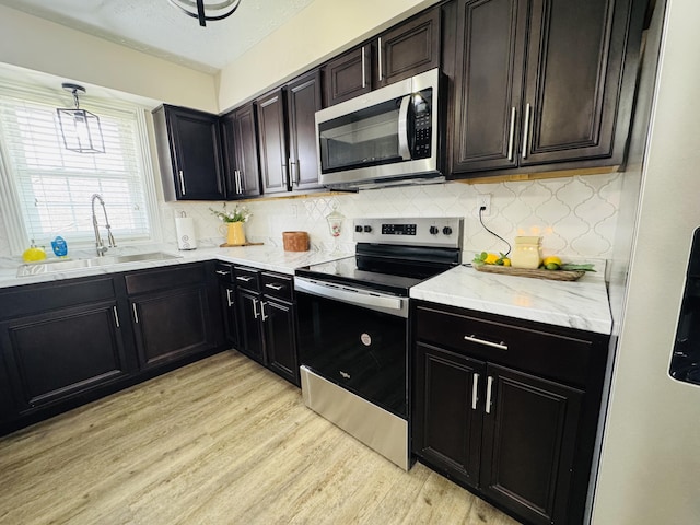 kitchen with light stone counters, decorative backsplash, appliances with stainless steel finishes, light wood-style floors, and a sink