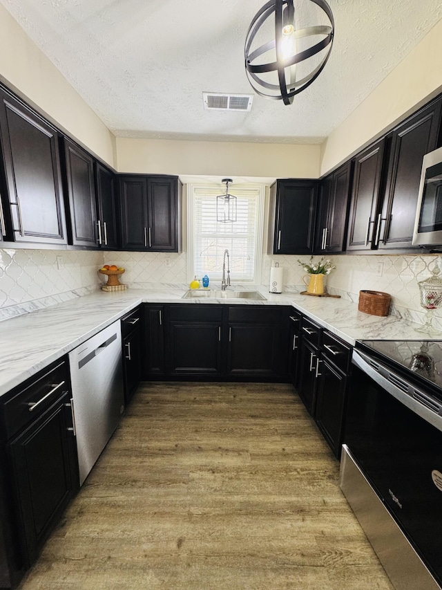 kitchen featuring light wood finished floors, visible vents, a sink, stainless steel appliances, and dark cabinets