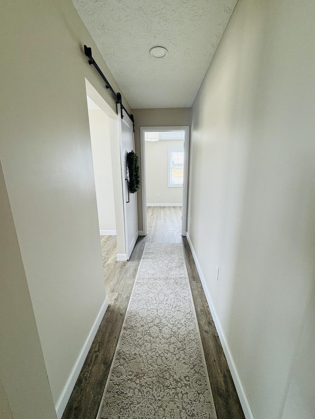 hall with a barn door, wood finished floors, baseboards, and a textured ceiling