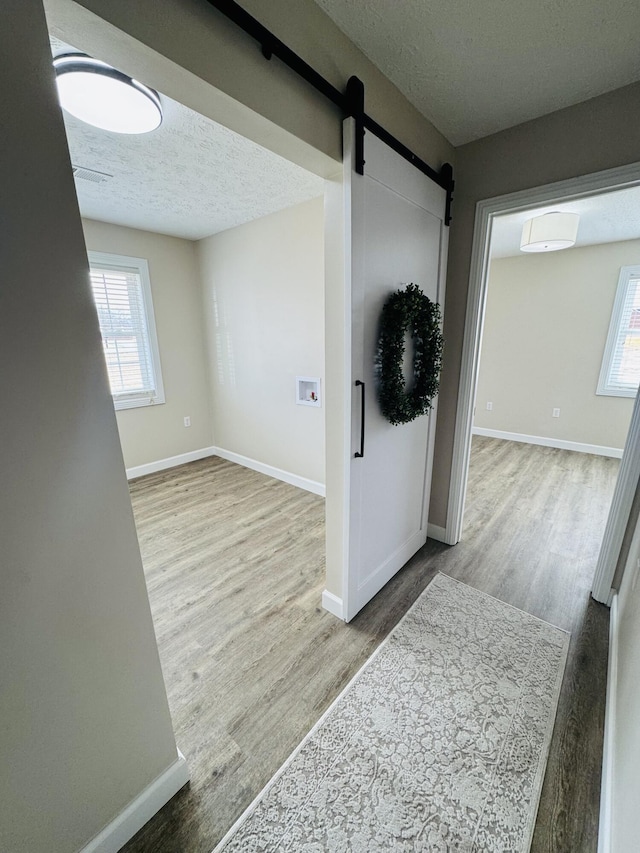 corridor featuring wood finished floors, a healthy amount of sunlight, and a textured ceiling