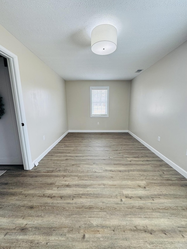 unfurnished room with visible vents, baseboards, a textured ceiling, and wood finished floors