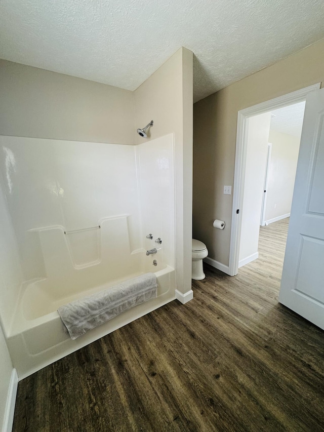 bathroom with toilet, a textured ceiling, wood finished floors, baseboards, and shower / bathtub combination