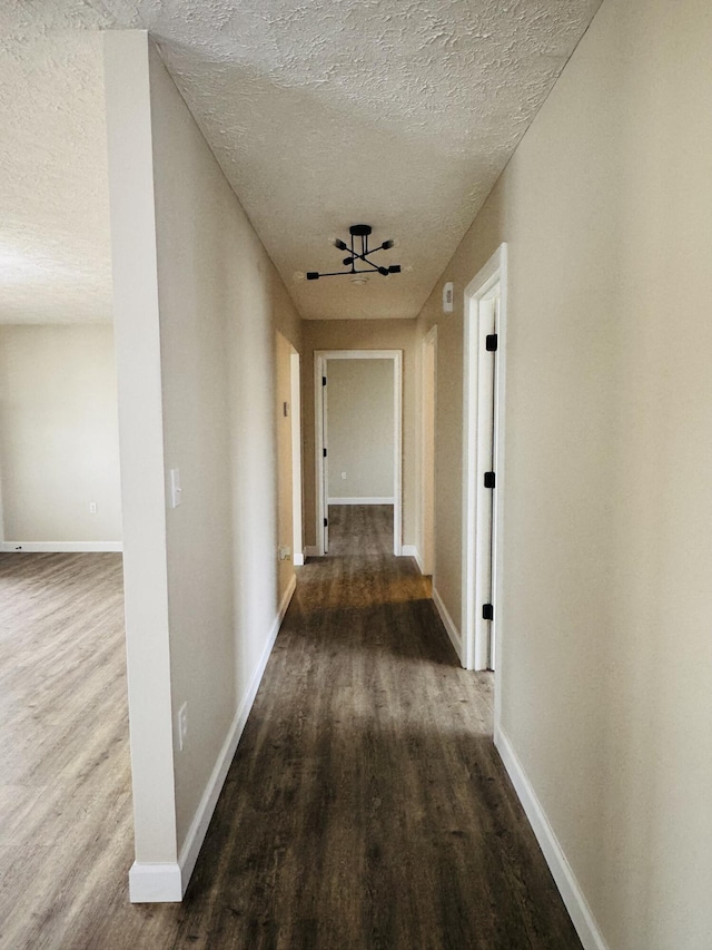 corridor with baseboards, a textured ceiling, and wood finished floors