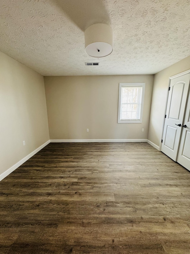 empty room featuring visible vents, a textured ceiling, dark wood-type flooring, and baseboards