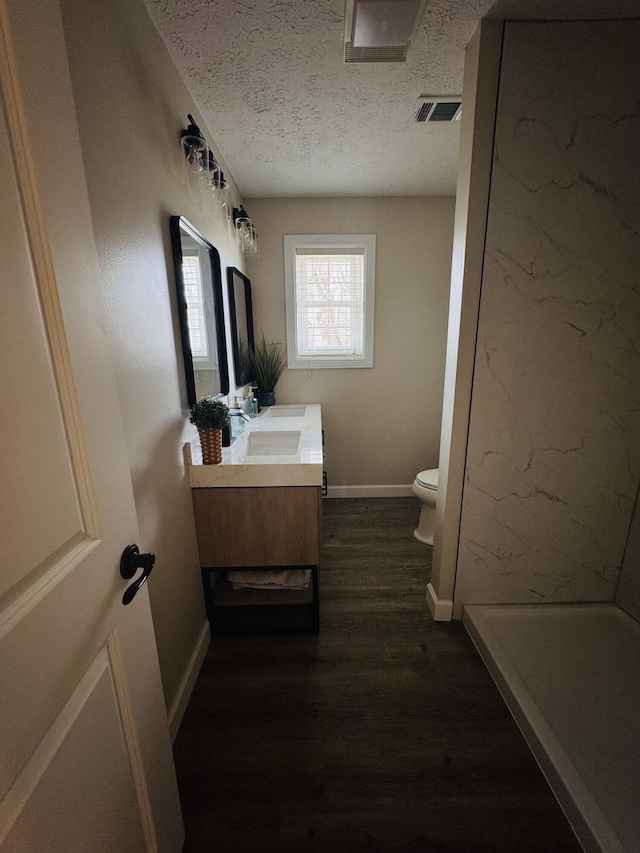 bathroom with toilet, a textured ceiling, wood finished floors, baseboards, and vanity