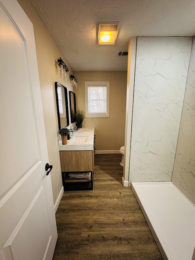 bathroom with visible vents, toilet, vanity, wood finished floors, and a textured ceiling