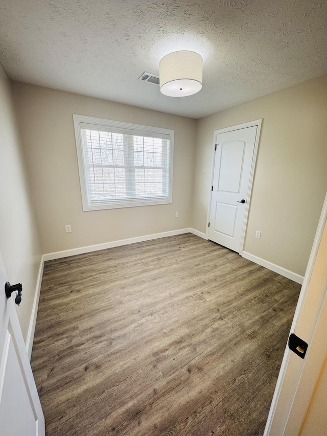 spare room featuring visible vents, a textured ceiling, baseboards, and wood finished floors