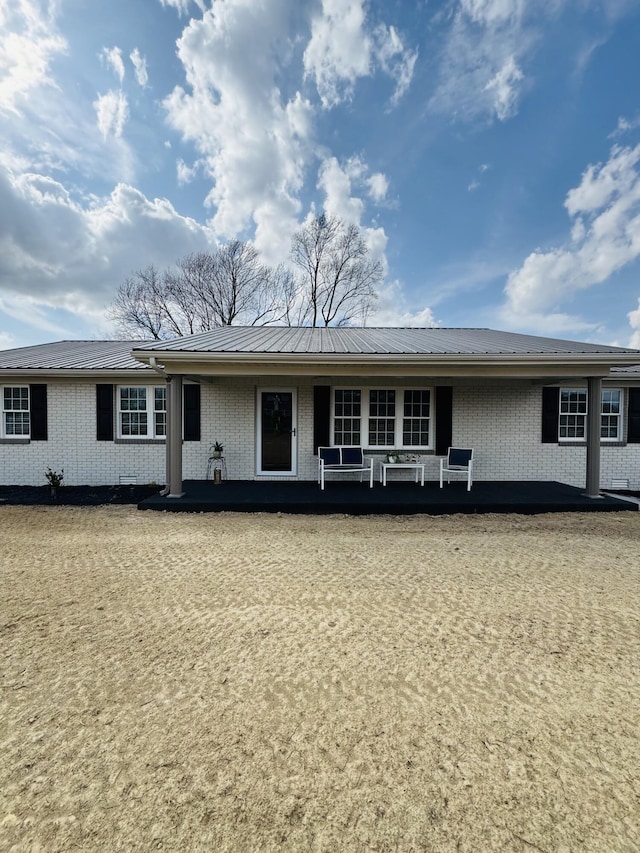 ranch-style house featuring brick siding, covered porch, and metal roof