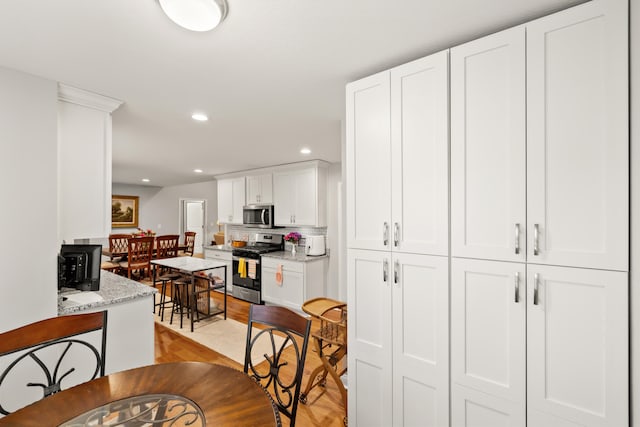 kitchen featuring tasteful backsplash, recessed lighting, appliances with stainless steel finishes, light wood-style flooring, and white cabinets