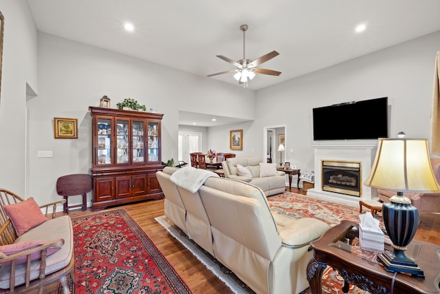 living area with recessed lighting, a fireplace with raised hearth, ceiling fan, and wood finished floors