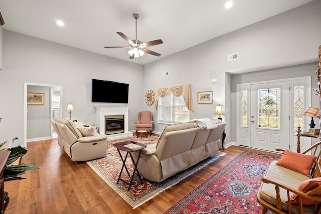 living room with visible vents, a fireplace with raised hearth, wood finished floors, and a ceiling fan