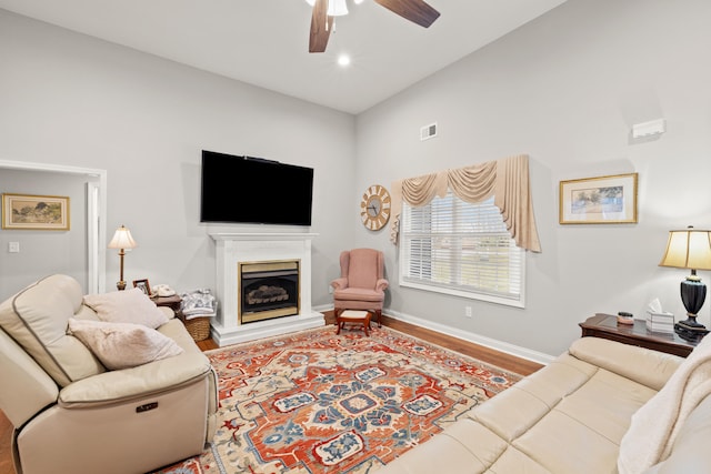 living room with wood finished floors, baseboards, visible vents, a fireplace with raised hearth, and ceiling fan