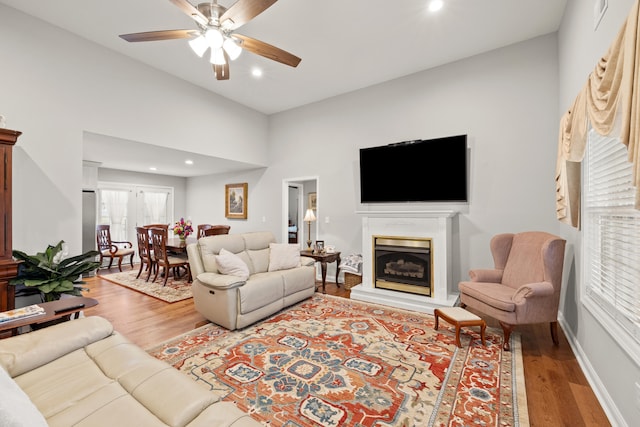 living room with a fireplace with raised hearth, wood finished floors, visible vents, and ceiling fan