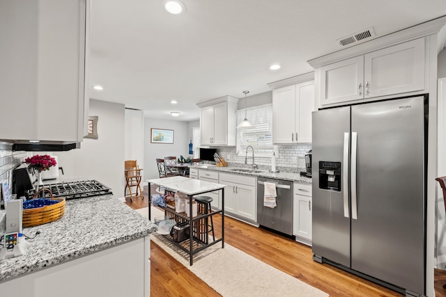 kitchen featuring visible vents, light wood finished floors, a sink, stainless steel appliances, and backsplash