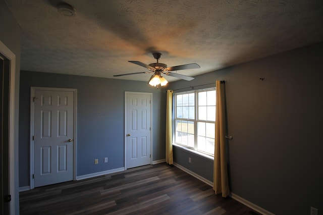 unfurnished bedroom featuring dark wood-style floors, a textured ceiling, baseboards, and a ceiling fan