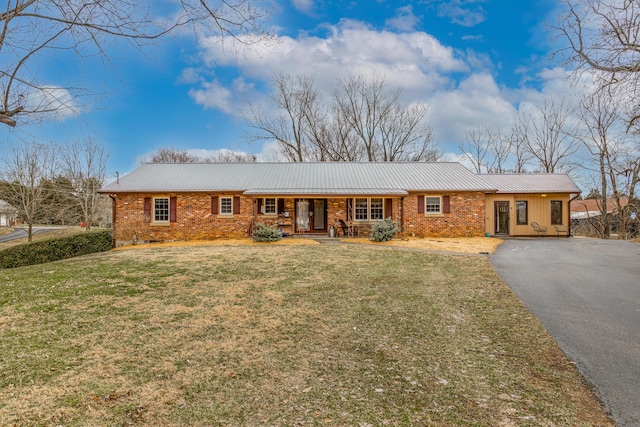 ranch-style home with brick siding, a porch, a front yard, metal roof, and driveway