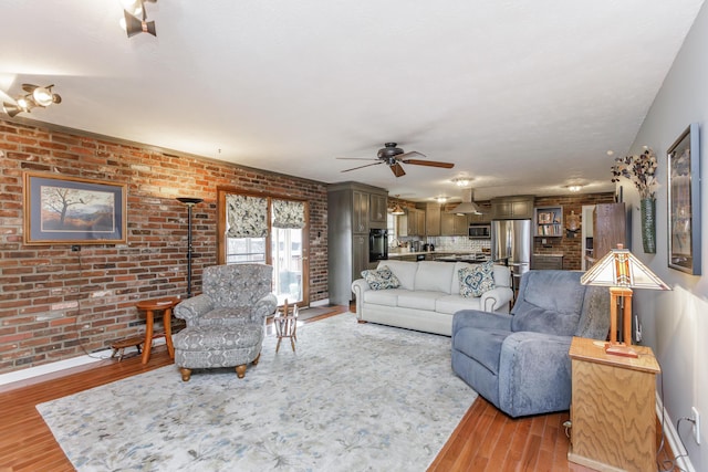 living area with baseboards, light wood-type flooring, brick wall, and ceiling fan