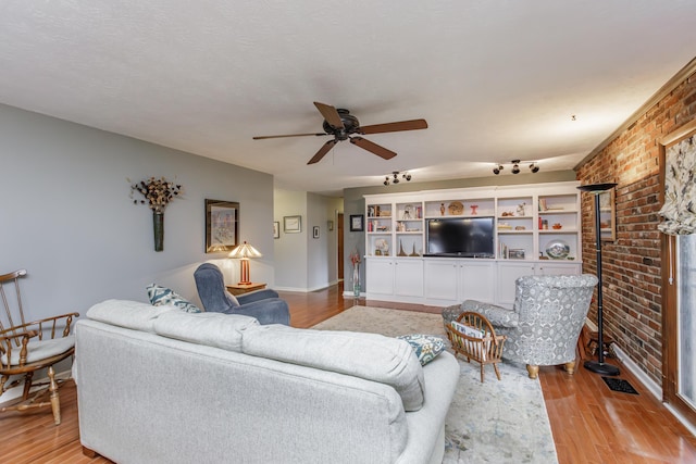 living area with visible vents, brick wall, baseboards, light wood-style flooring, and a ceiling fan