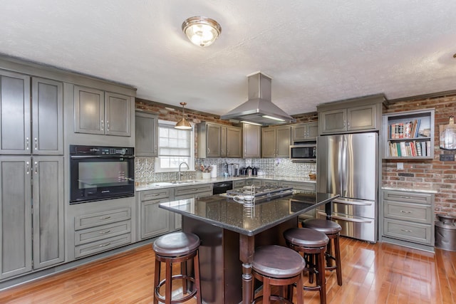 kitchen with a sink, black appliances, a kitchen bar, and island range hood