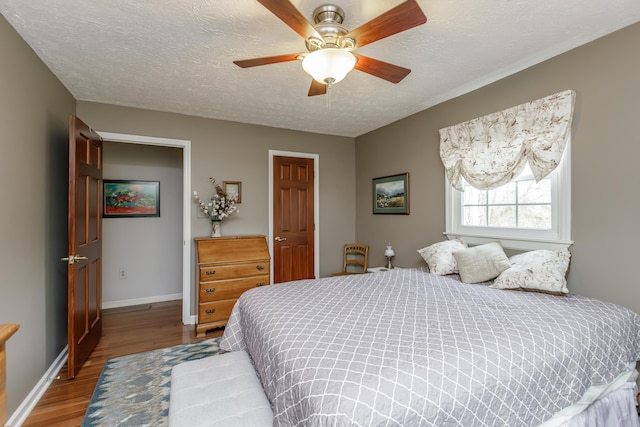 bedroom with ceiling fan, a textured ceiling, baseboards, and wood finished floors