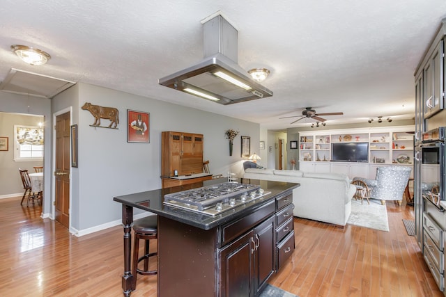 kitchen with island exhaust hood, a kitchen breakfast bar, a textured ceiling, light wood finished floors, and stainless steel gas cooktop