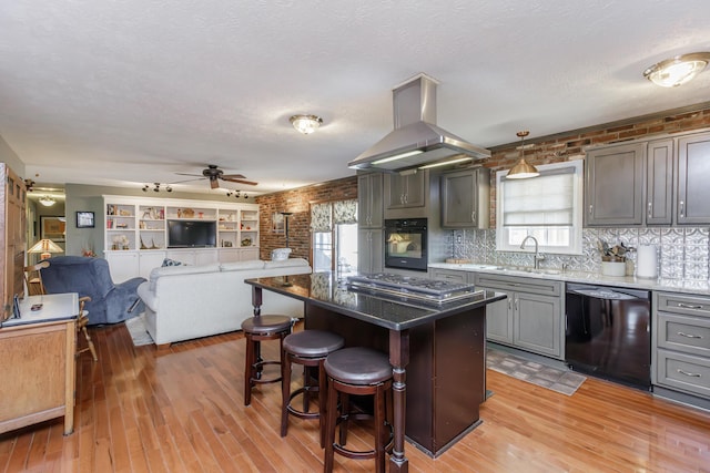 kitchen with black appliances, island exhaust hood, a sink, light wood-style floors, and a breakfast bar area