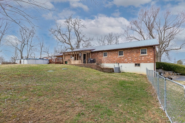 rear view of property featuring metal roof, brick siding, a yard, and fence