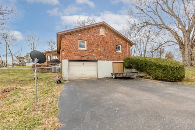 view of side of home featuring brick siding, an attached garage, driveway, and fence