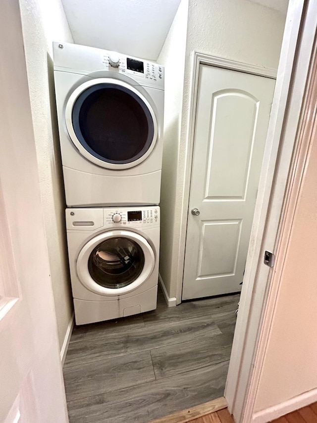 washroom with laundry area, wood finished floors, baseboards, and stacked washer and dryer