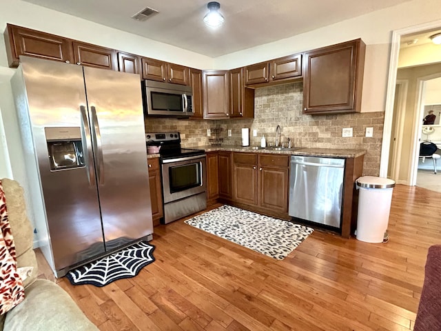 kitchen with tasteful backsplash, visible vents, light wood-type flooring, stainless steel appliances, and a sink