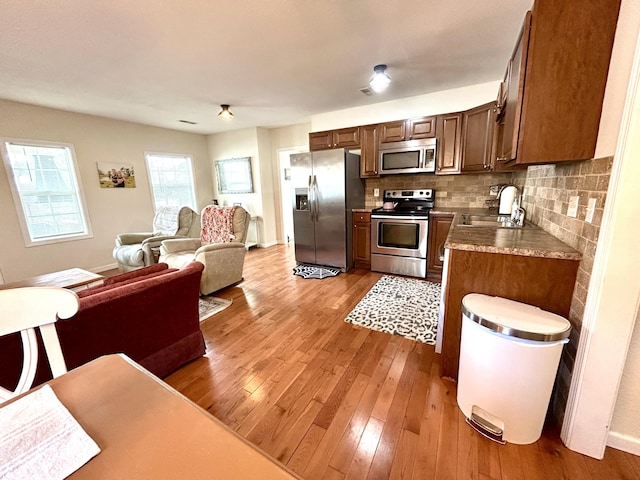 kitchen with backsplash, open floor plan, hardwood / wood-style floors, appliances with stainless steel finishes, and a sink